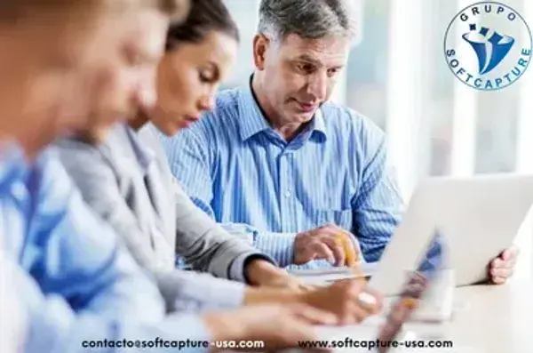 Tres personas trabajan frente a sus computadores en una mesa compartida.