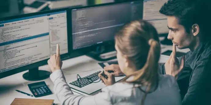 Dos personas revisan código en pantalla; una señala una línea.